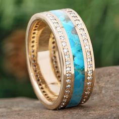 a gold ring with turquoise and white stones on it sitting on top of a rock