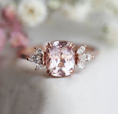 a pink diamond ring sitting on top of a white table with flowers in the background