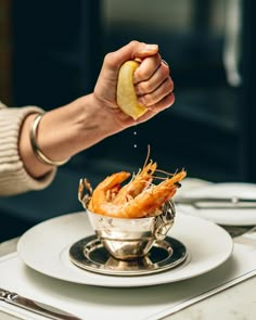 a person is sprinkling some food on top of a silver bowl with shrimp in it