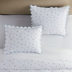 two white pillows on top of a bed next to each other with blue stars and scalloped edges