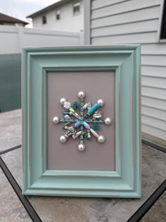 a snowflake made out of beads is displayed in a frame on a table