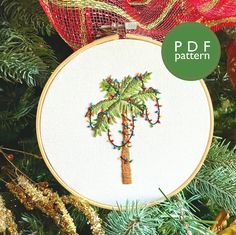 a cross stitch palm tree is hanging on a christmas tree with red and gold ornaments