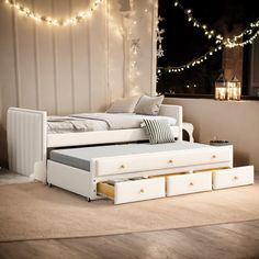 a white bed with drawers underneath it in a room filled with lights and string lights