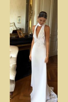 a woman wearing a white dress standing in front of a table with a mirror on it