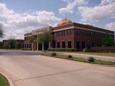 an empty street in front of a brick building with a dome on top and trees around it