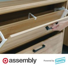 a person is opening the drawer on a wooden desk with an assembly logo in the background