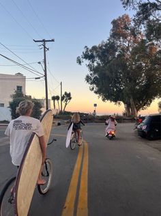 two people riding bikes with surfboards on their backs and one person holding a skateboard