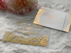 two gold and silver wedding cards on white furnishing with pink flowers in the background