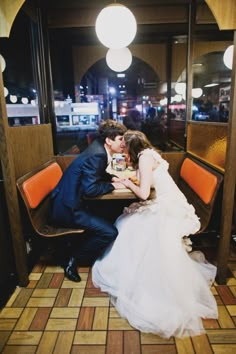 a bride and groom sitting at a table in a restaurant, sharing a kiss on the cheek