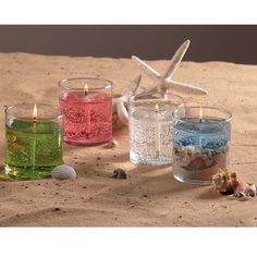 three different colored candles sitting on top of a sandy beach next to shells and starfish