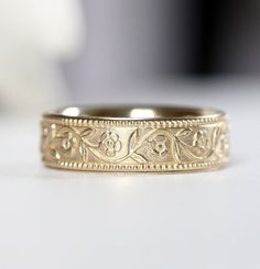 a gold wedding band with an intricate design on the outside and inside, sitting on a white surface