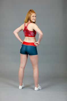 a woman with red hair and blue shorts is standing in front of a gray background