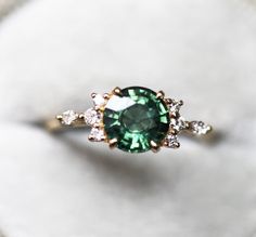 a green and white diamond ring sitting on top of a marble surface with diamonds around it