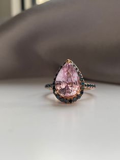 a pink and black diamond ring sitting on top of a table