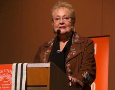 an older woman standing at a podium in front of a microphone