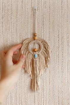 a hand holding a beaded and tasseled wall hanging on a beige carpet