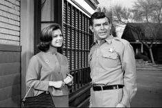 a man and woman standing next to each other in front of a building with large windows