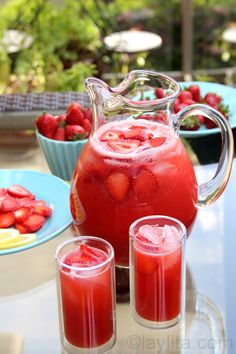 a pitcher of water with strawberries in it and three glasses filled with juice on the table