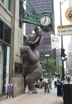 an elephant statue in the middle of a city street next to a clock and taxi sign