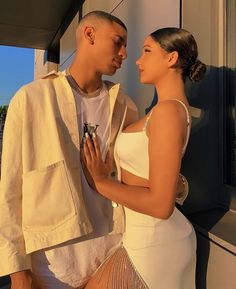 a man and woman standing next to each other in front of a window looking at each other