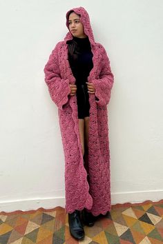 a woman standing in front of a white wall wearing a pink coat and black dress