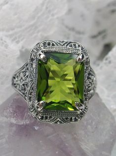 Simulated Green Peridot Ring Autumn Design #D200 Inspired by Victorian era designs, this lovely filigree reproduction has been recreated in sterling silver. This flawless 5 carat simulated Green Peridot gemstone is 12mm x10mm in size. The ring sits 17mm (11/16") North to South on the finger. The inside of the band is etched 925 for sterling silver. Notice the intricate and detailed design of the antique silver filigree setting all the way down the band. This is an exquisite rendition of an antiq Classic Peridot Jewelry With Accent Stones, Classic Green Filigree Ring With Gemstone, Elegant Rectangular Peridot Rings, Elegant Filigree Ring For May Birthstone, Classic Peridot Jewelry For Formal Occasions, Classic Green Filigree Ring Hallmarked, Green Sterling Silver Classic Filigree Ring, Classic Green Sterling Silver Filigree Ring, Classic Filigree Ring With Emerald Cut For Gift