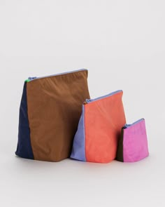 three different colored bags sitting next to each other on a white surface with one bag in the middle