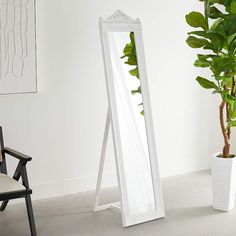 a white floor standing mirror next to a potted plant