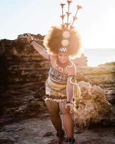 a woman with an afro is dancing on the rocks by the ocean in her native clothing