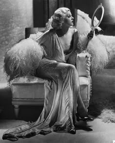 an old photo of a woman sitting on a chair holding a tennis racquet