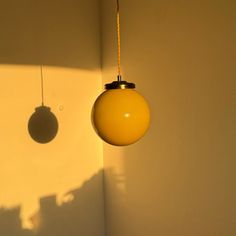 a yellow light hanging from a ceiling in a room with white walls and shadows on the wall