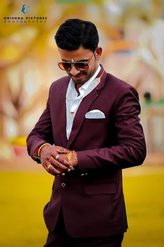 a man in a maroon suit and white shirt is looking down at his hand while wearing sunglasses