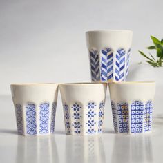 four blue and white cups sitting next to each other on top of a table with a plant in the background