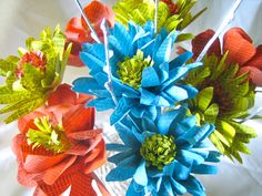 an arrangement of colorful paper flowers on a white tablecloth with red, green and blue ribbons