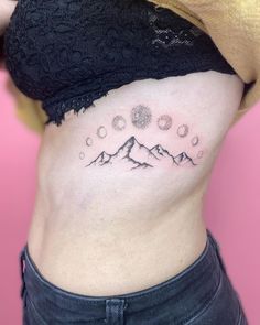 a woman's stomach with mountains and stars tattoo on her left side ribcage