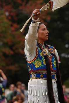 a native american woman holding a feather in her hand and wearing a colorful outfit with feathers on it