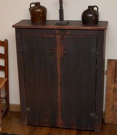 an old wooden cabinet with two vases on top and a chair next to it