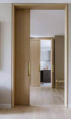 an open door leading to a kitchen and living room with white walls, wood floors and wooden doors