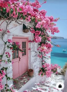 pink door and flowers on the side of a white building with blue water in the background