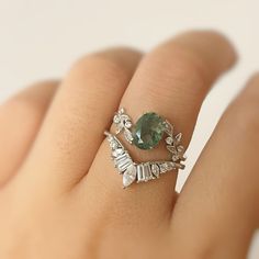 a woman's hand holding a ring with an oval green stone and leaves on it