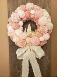 a pink and white wreath with pom - poms hanging on a wooden door