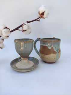 two cups and saucers sitting next to each other on a white surface with cotton in the background