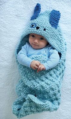 a baby wrapped in a crocheted blanket with a blue dragon on it's back