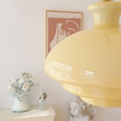 a yellow light hanging from the ceiling in a room with white vases and pictures on the wall