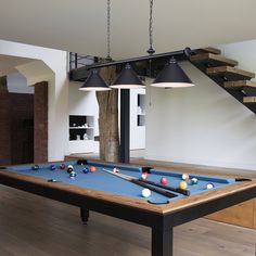 a pool table in the middle of a living room with stairs leading up to it