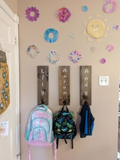 two backpacks are hanging on the wall next to some hooks with letters and flowers