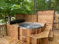 a hot tub sitting on top of a wooden deck next to a wooded area with benches