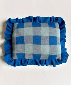 a blue and gray checkered pillow with ruffles on the bottom, sitting on a white surface