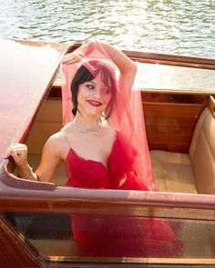 a woman in a red dress is sitting in a boat with a veil over her head