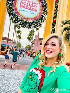 a woman standing in front of the universal studios holiday parade sign with her hand on her hip